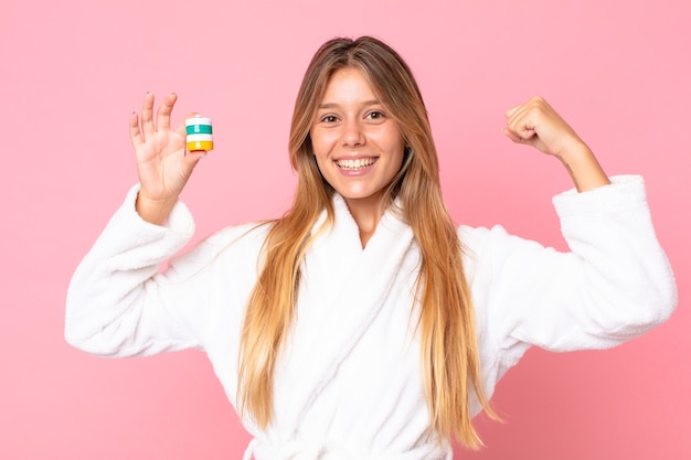 Jolie jeune femme blonde portant un peignoir et tenant un produit cosmétique