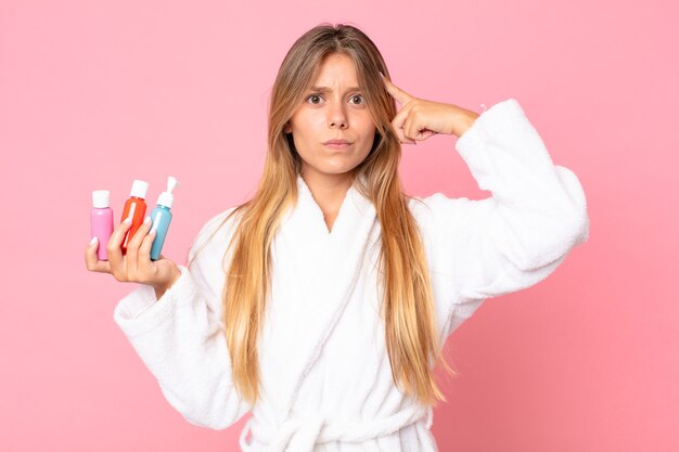 Jolie jeune femme blonde portant un peignoir et tenant un produit cosmétique