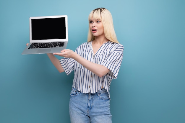 Une jolie jeune femme blonde en tenue décontractée démontre l'écran d'un ordinateur portable avec une maquette