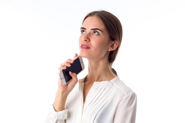 Jolie jeune femme en blouse blanche tenant son téléphone portable rose sur fond blanc en studio