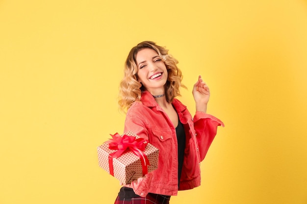 Jolie jeune femme avec boîte-cadeau sur fond de couleur