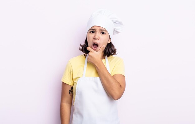 Jolie jeune femme avec la bouche et les yeux grands ouverts et la main sur le menton. concept de chef