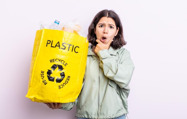 Jolie jeune femme avec la bouche et les yeux grands ouverts et la main sur le menton. concept de recyclage du plastique