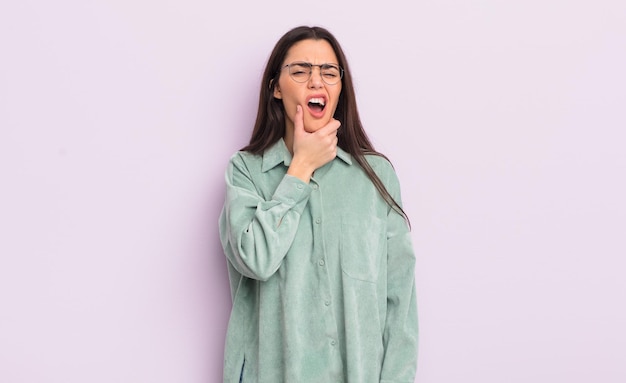 Jolie jeune femme avec la bouche et les yeux grands ouverts et la main sur le menton se sentant désagréablement choquée de dire quoi ou wow