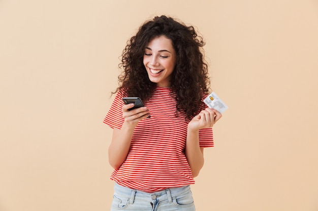 Jolie jeune femme bouclée à l'aide de téléphone portable tenant une carte de crédit.