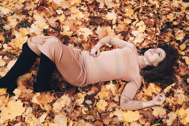 Jolie jeune femme brune allongée sur les feuilles d'automne jaunes à l'extérieur. Fille avec des feuilles. Vue d'en haut, dans le parc en automne.