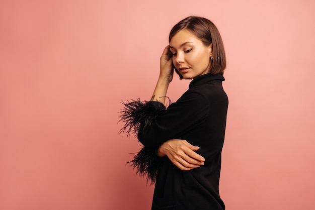 Jolie jeune femme brune caucasienne avec coupe de cheveux bob dans des vêtements noirs regarde ailleurs tout en se tenant sur fond rose Sweet home concept de vie réelle