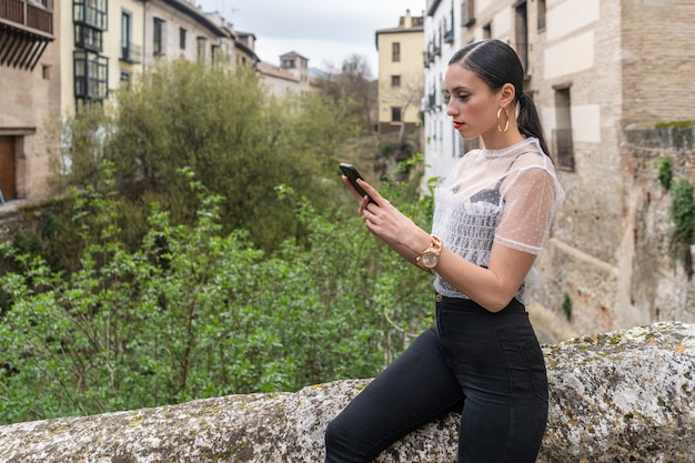 Jolie jeune femme brune caucasienne regardant le smartphone dans des vêtements noirs et blancs