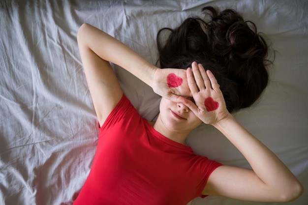 Jolie jeune femme brune avec dessin coeur sur les mains dans le lit