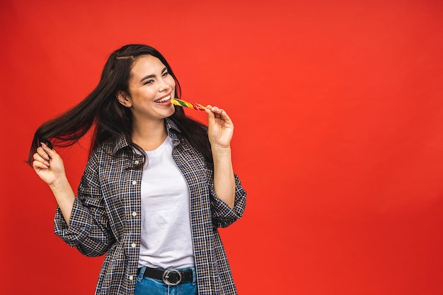 Jolie jeune femme brune heureuse souriante avec sucette isolé sur fond rouge