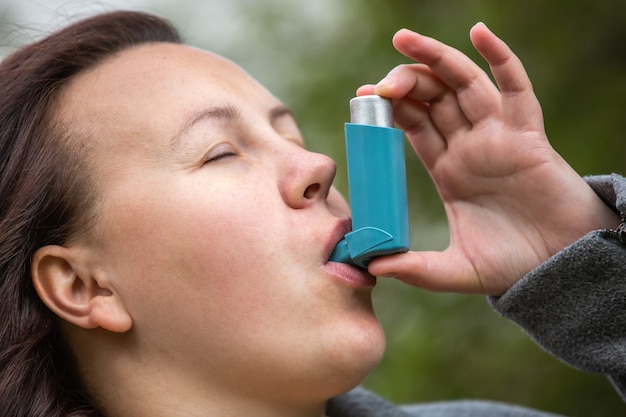 Photo jolie jeune femme brune utilisant un inhalateur pour l'asthme lors d'une forte crise d'asthme le produit pharmaceutique est utilisé pour prévenir et traiter la respiration sifflante et l'essoufflement