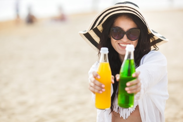 Jolie jeune femme buvant un cocktail sur la plage. Jolie fille offrant un verre. Belle femme buvant de la limonade