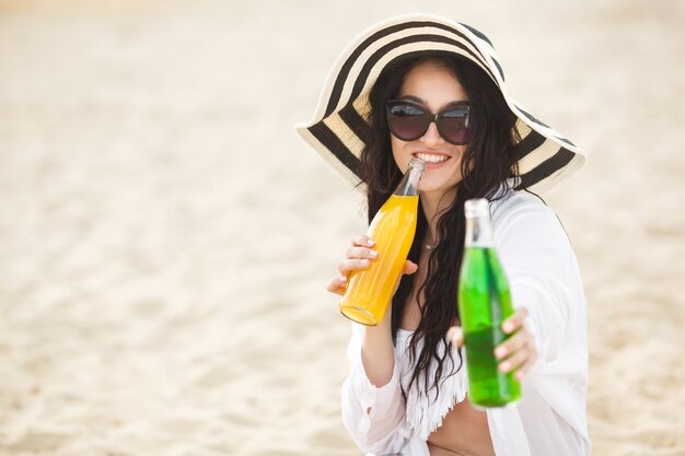 Jolie jeune femme buvant un cocktail sur la plage. Jolie fille offrant un verre. Belle femme buvant de la limonade