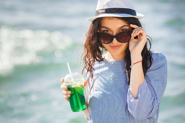 Jolie jeune femme buvant un cocktail sur la plage. Jolie fille offrant un verre. Belle femme buvant de la limonade