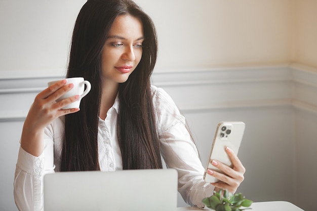 Jolie jeune femme à la cafétéria tapant sur ordinateur portable Brunette à l'intérieur avec des gadgets