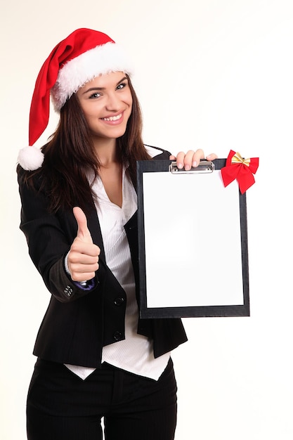 Jolie jeune femme en cap Santa's avec presse-papiers sur fond blanc