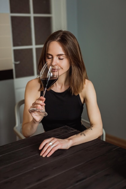 Une jolie jeune femme caucasienne dégustant un verre de vin rouge assis à la table en bois de la cuisine