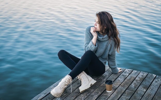 Une jolie jeune femme en chandail est assise au bord de la rivière