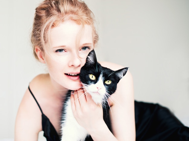 Jolie jeune femme avec chat noir en couverture dans la chambre blanche