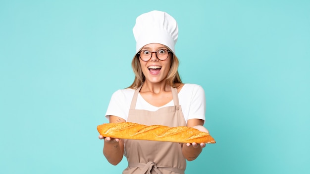 Jolie jeune femme chef blonde tenant une baguette de pain