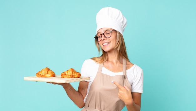 Jolie jeune femme chef blonde tenant un plateau de croissants