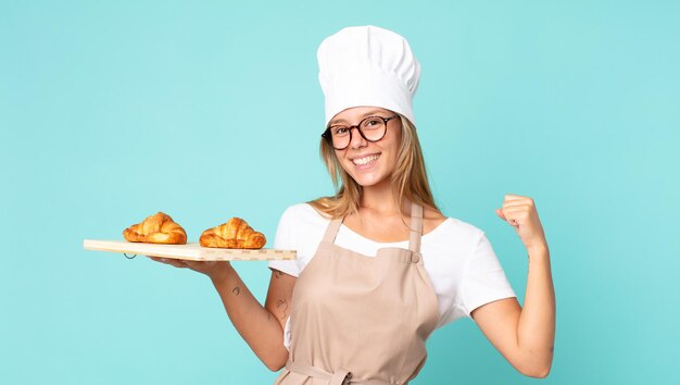 Jolie jeune femme chef blonde tenant un plateau de croissants