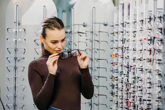 Jolie jeune femme choisit de nouvelles lunettes au magasin d'optique.