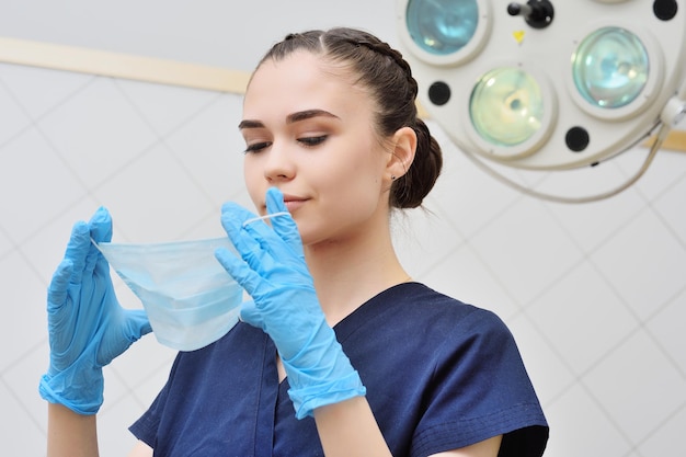 Jolie jeune femme en costume chirurgical met un masque stérile