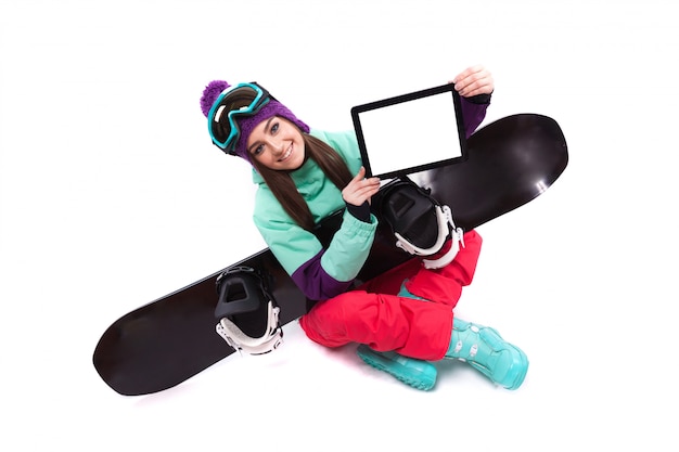 Jolie jeune femme en costume de ski violet, implantation en tailleur, tablette vide