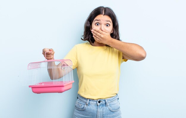 Jolie jeune femme couvrant la bouche avec les mains avec un choc. concept de cage pour animaux de compagnie