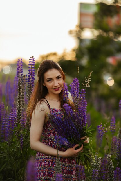 Jolie jeune femme dans un champ au coucher du soleil. tenant des fleurs