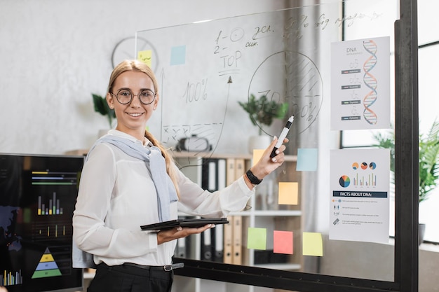 Jolie jeune femme debout près d'une planche de verre avec divers graphiques et tableaux