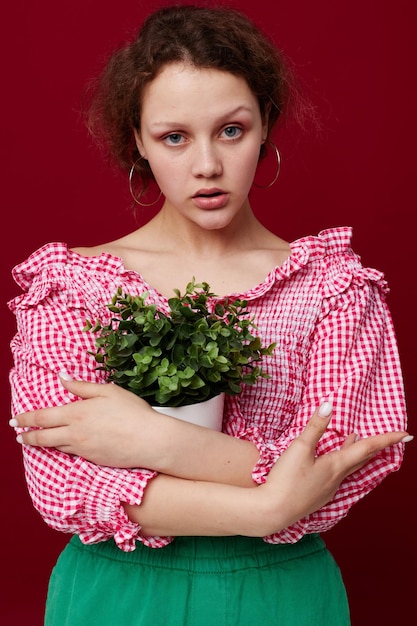 Jolie jeune femme debout et tenant une fleur en pot fond rouge