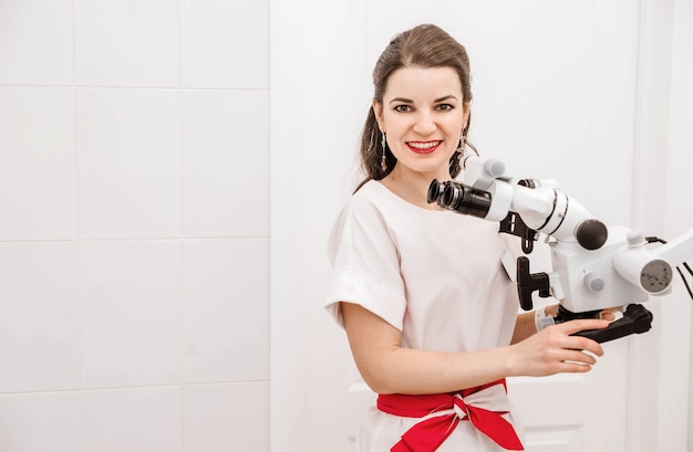 Jolie jeune femme dentiste dans un costume blanc à l'aide d'un microscope