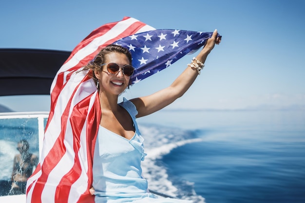Jolie jeune femme avec le drapeau national américain s'amusant et passant la journée sur son yacht privé.