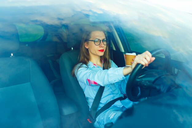 Photo une jolie jeune femme avec du café pour conduire sa voiture.