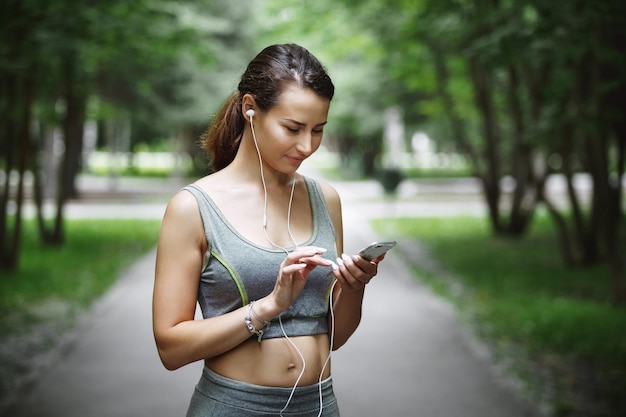 Jolie jeune femme écoutant de la musique tout en faisant du jogging sur le chemin dans un parc verdoyant