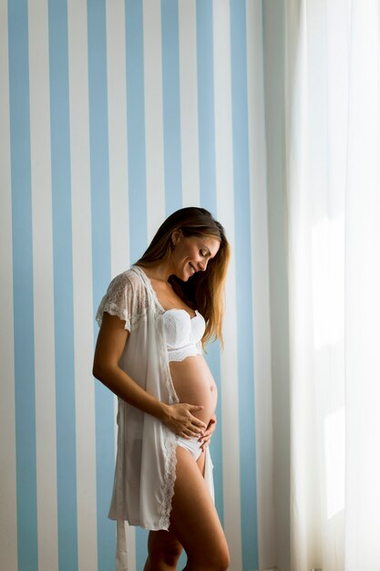 Jolie jeune femme enceinte debout près du mur bleu dépouillé de la chambre