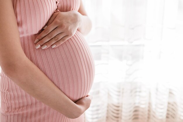 Une jolie jeune femme enceinte debout près de la fenêtre de la maison