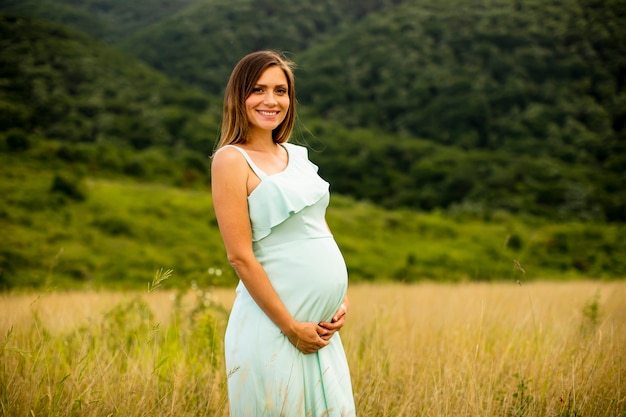 Jolie jeune femme enceinte se détendre à l'extérieur dans la nature au jour d'été