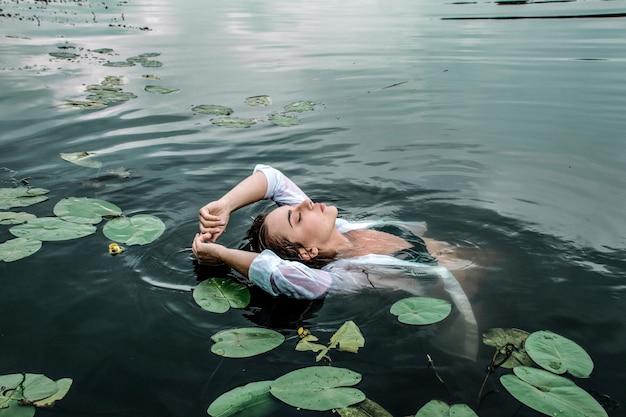 Jolie jeune femme enchanteresse nageant dans un lac parmi de beaux nénuphars.