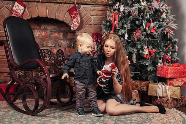 Jolie jeune femme avec un enfant d'un an jouant près de l'arbre de Noël