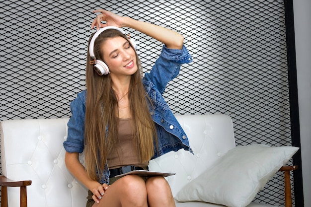 Jolie Jeune Femme Est Assise Sur Le Canapé Et Porte Un Casque Pour écouter De La Musique Depuis Une Tablette