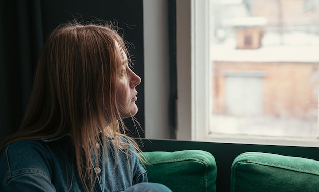 Une jolie jeune femme est assise sur le canapé près de la fenêtre