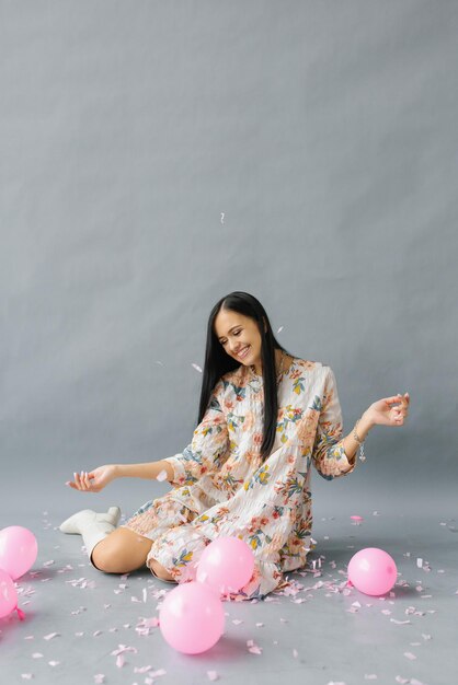 Une jolie jeune femme est assise près de ballons roses et jette des confettis et des sourires