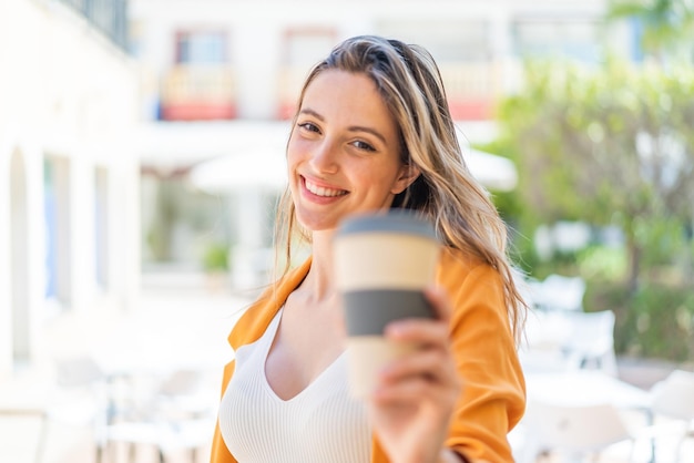 Une jolie jeune femme à l'extérieur tenant un café à emporter avec une expression heureuse