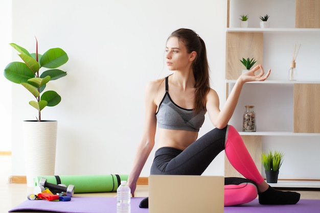 Jolie jeune femme faisant du yoga qui s'étend du yoga en ligne à la maison