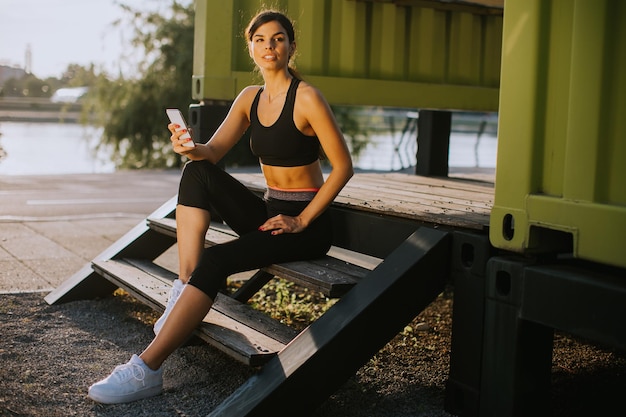 Jolie jeune femme faisant une pause pendant l'exercice à l'extérieur et à l'aide de téléphone portable