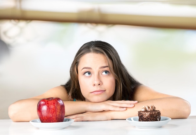 Jolie jeune femme fait son choix entre pomme et gâteau, concept de mode de vie sain