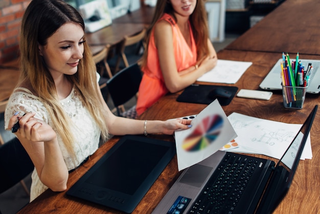 Jolie jeune femme graphiste à la recherche de nuancier assis à son bureau dans son bureau